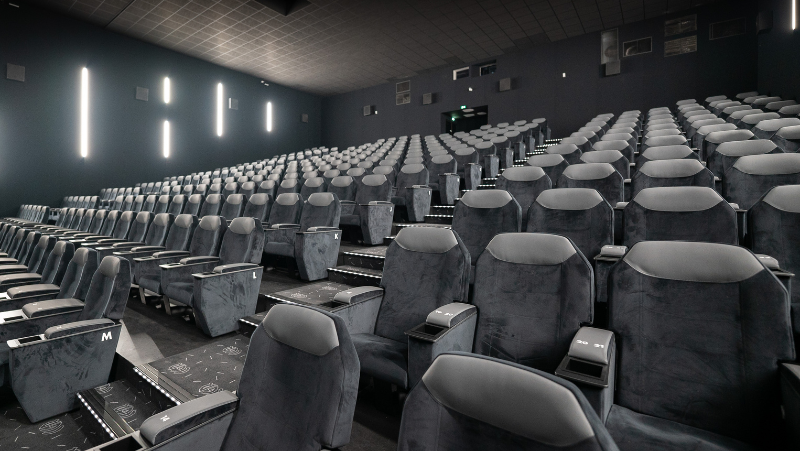 Salle de cinéma CGR vide avec fauteuils gris haut de gamme et éclairage mural blanc